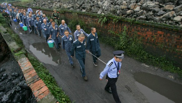 A policeman leads inmates as they walk along a road with their wrists tied together to a rope at Emei Mountain region